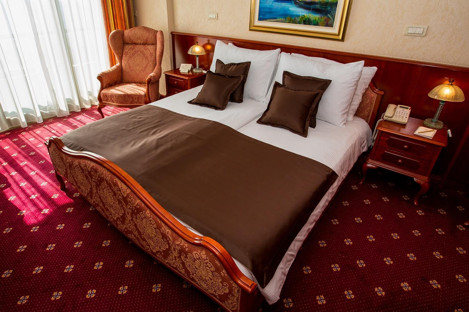 Grand Hotel Bernardin Portorose Esterno foto The photo shows a well-decorated bedroom featuring a large bed with a light-colored headboard and neatly arranged white linens. The bed is adorned with a brown bedspread and decorative pillows. On either side of the bed, there are wooden nightstands 