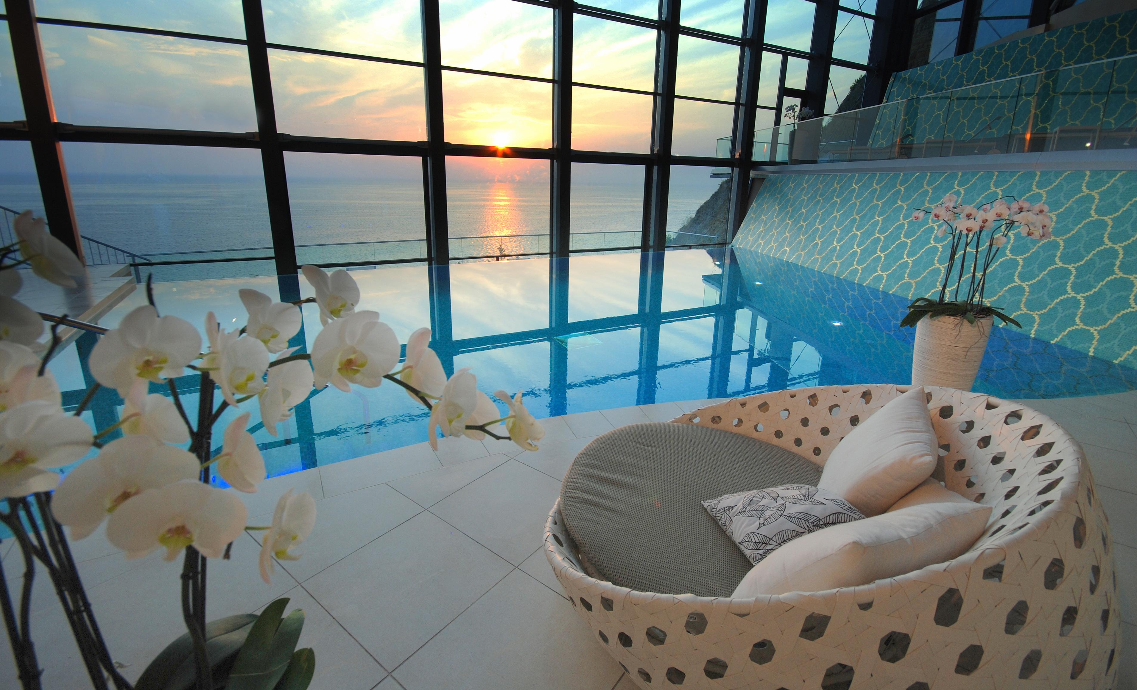 Grand Hotel Bernardin Portorose Esterno foto The photo shows an elegant indoor space featuring a swimming pool with a panoramic view of the ocean at sunset. The pool reflects the colors of the sunset, creating a serene atmosphere. In the foreground, there is a comfortable, uniquely designed cha
