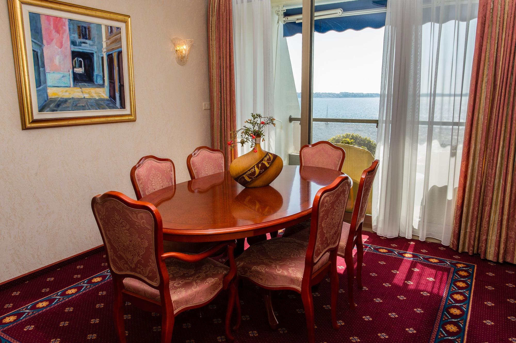 Grand Hotel Bernardin Portorose Esterno foto The photo shows an elegant dining area with a wooden round table surrounded by six upholstered chairs. The chairs have a decorative pattern and are positioned around the table. A small vase with flowers sits at the center of the table. In the backgro