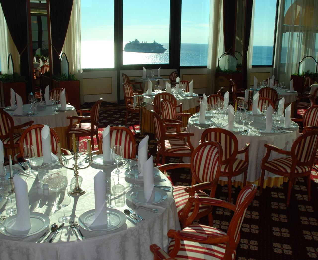 Grand Hotel Bernardin Portorose Esterno foto The photo shows an elegant dining area with several round tables adorned with white tablecloths. Each table is set with dishes, cutlery, and folded white napkins. The decor features wooden chairs with a striped pattern. Large windows provide a view o