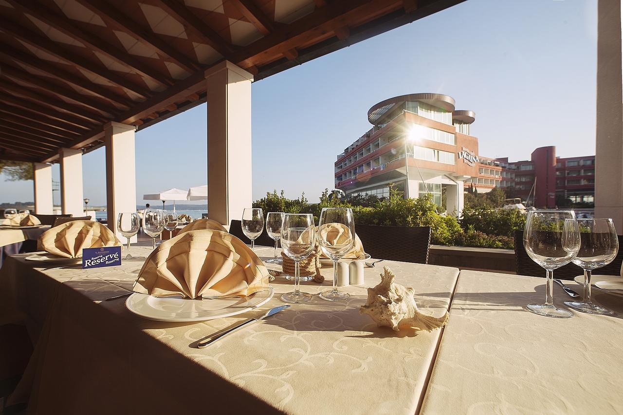 Grand Hotel Bernardin Portorose Esterno foto The photo depicts a dining setup at a restaurant, featuring elegantly arranged tables on a terrace. Each table is covered with a light-colored tablecloth and has an artistic napkin folding resembling a flower. There are several empty wine glasses and