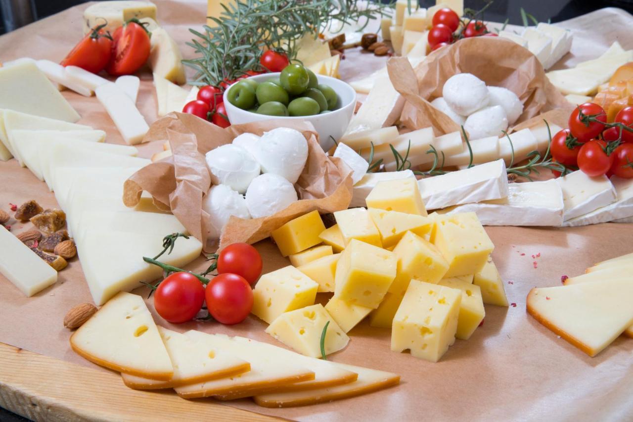 Grand Hotel Bernardin Portorose Esterno foto The photo features a beautifully arranged cheese platter that includes various types of cheese, such as sliced yellow cheese, brie, and small balls of fresh mozzarella. Accompanying the cheese are green olives, cherry tomatoes, and sprigs of fresh ro