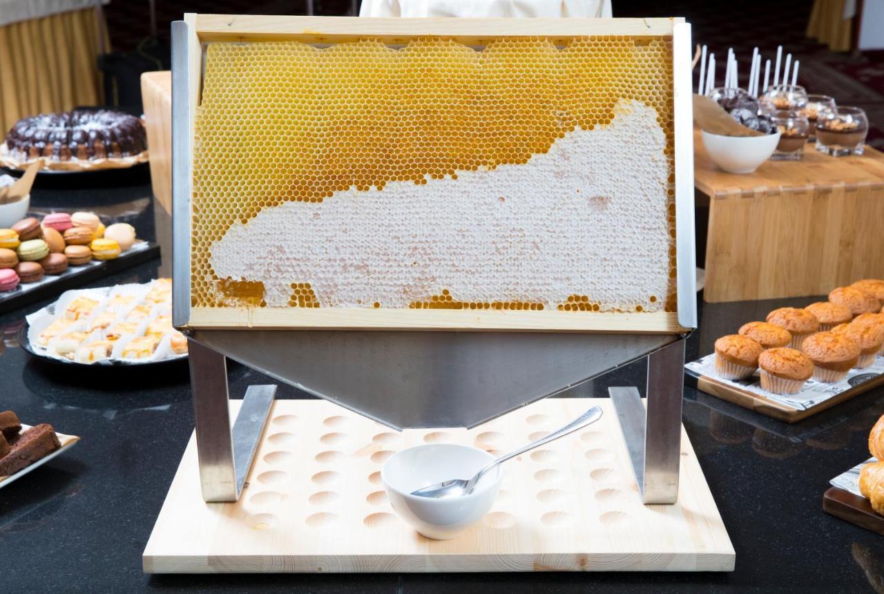 Grand Hotel Bernardin Portorose Esterno foto The photo shows a honeycomb displayed on a stand, with honey oozing from the cells. The honeycomb is mounted vertically, allowing a view of its hexagonal structure. Below the honeycomb, there is a white bowl and a spoon positioned on a wooden base. I