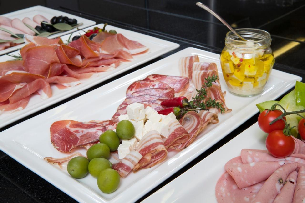 Grand Hotel Bernardin Portorose Esterno foto The photo shows a selection of charcuterie and accompaniments arranged on white plates. There are various types of cured meats, including slices of ham and salami, presented attractively. In the center, there are green olives and pieces of cheese, al