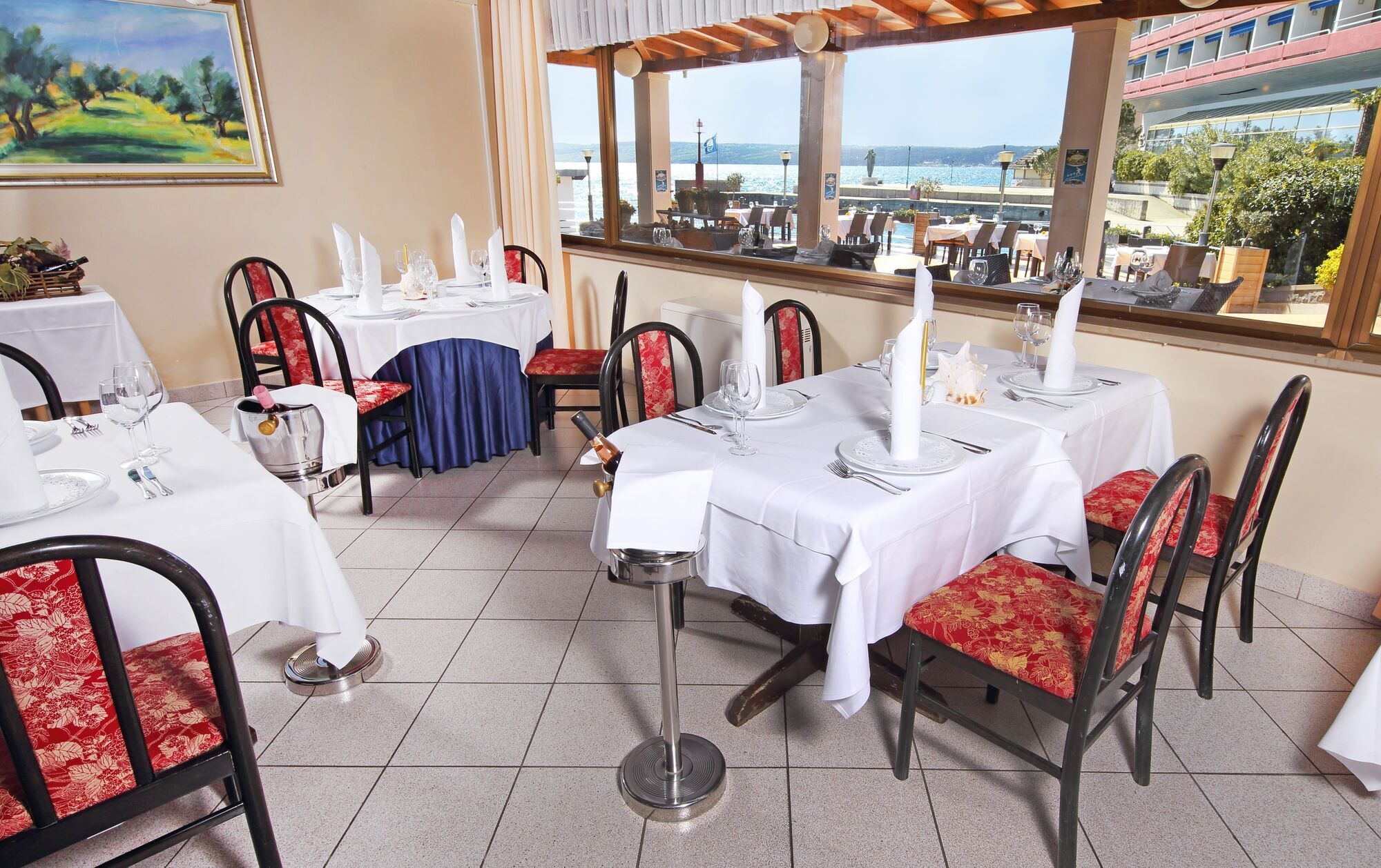 Grand Hotel Bernardin Portorose Esterno foto The photo shows the interior of a dining area in a restaurant. There are several tables, each covered with white tablecloths. The chairs are a mix of black frames with either floral or solid-colored cushions. Large windows provide a view of the outsi